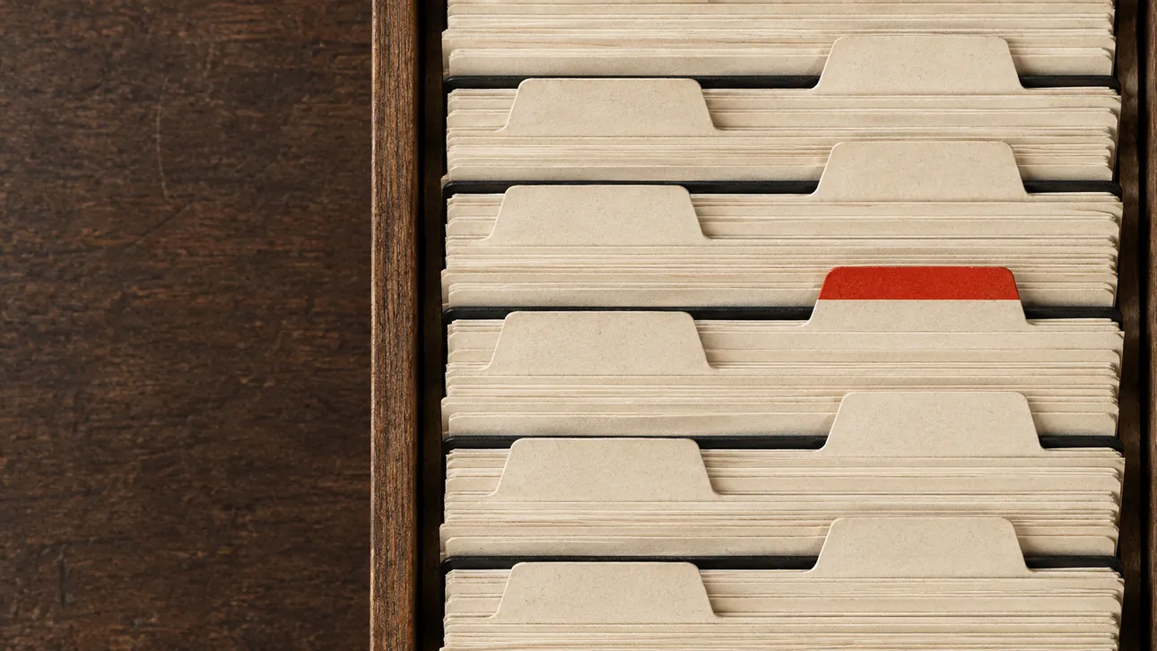 An index card filing drawer photographed from above, rows of blank cards with one tab marked in red